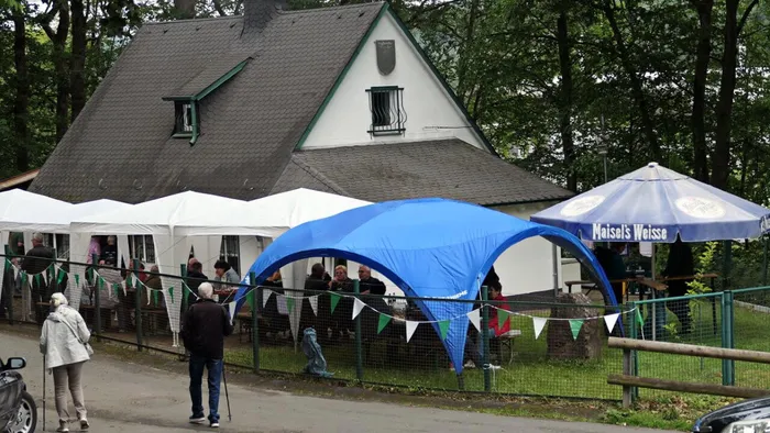 Menschen sitzen unter Pavillons und Sonnenschirmen vor einem Fachwerkhaus, das Räucherfest des Anglerclubs Forelle Eiringhausen.