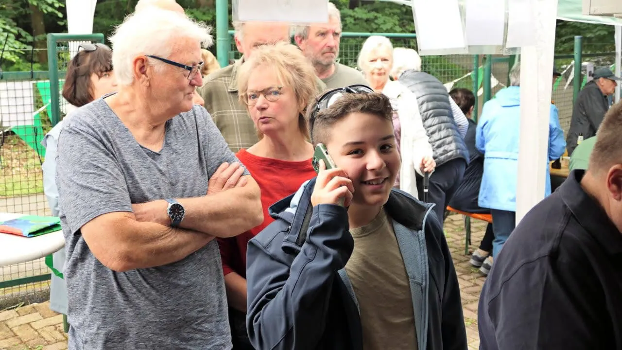 Ein Junge telefoniert während eines Räucherfestes des Anglerclubs Forelle Eiringhausen, umgeben von anderen Besuchern.