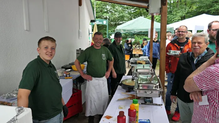 Mitarbeiter des Anglerclubs Forelle Eiringhausen bedienen Besucher an einem Büfett mit Räucherfisch und Beilagen im Freien.
