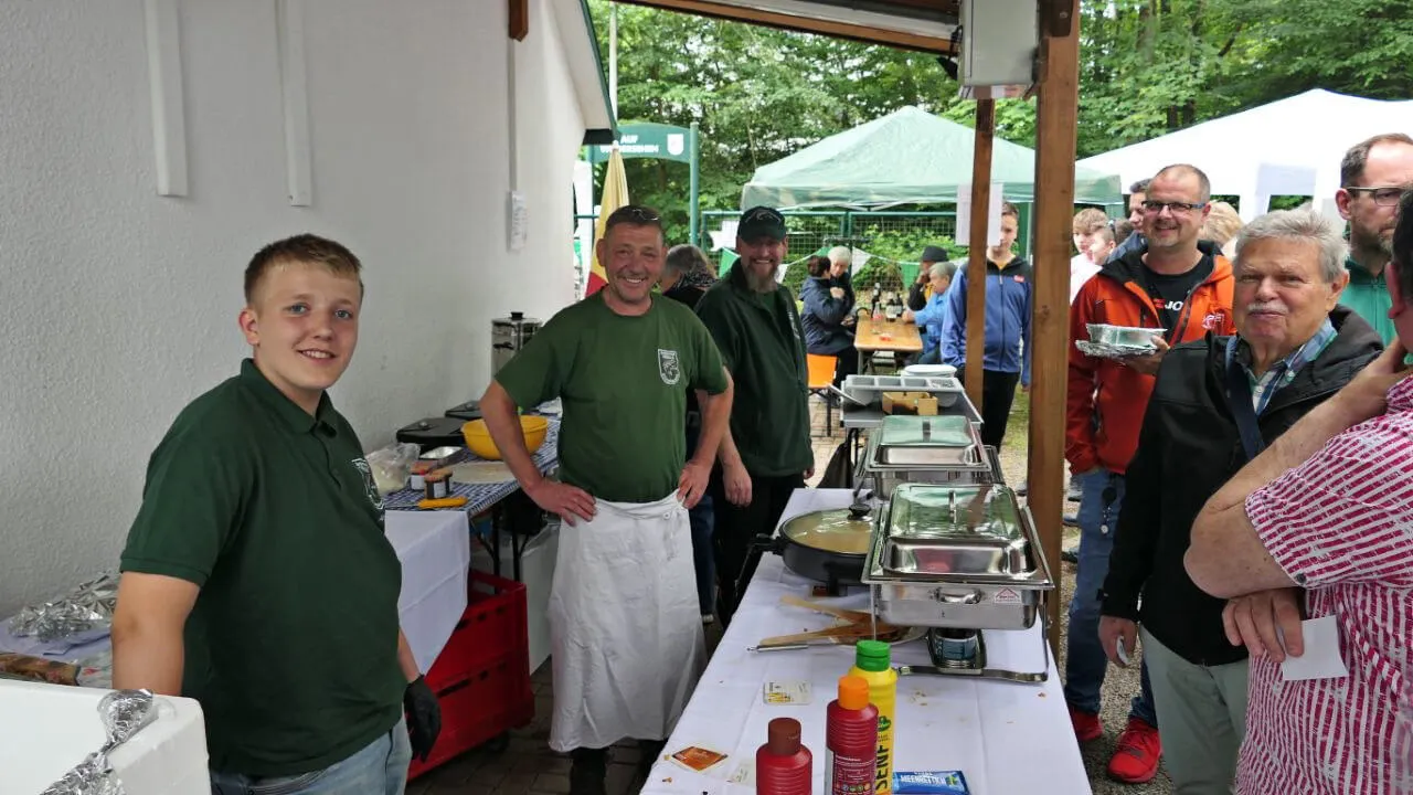 Mitarbeiter des Anglerclubs Forelle Eiringhausen bedienen Besucher an einem Büfett mit Räucherfisch und Beilagen im Freien.
