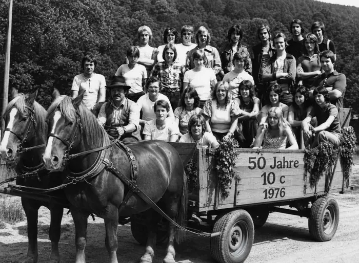 Schwarz-Weiß-Foto von einem Klassentreffen des Abschlussjahrgangs 1976 der Realschule Plettenberg. Eine Gruppe junger Menschen sitzt und steht auf einem mit Blumen geschmückten Wagen, der von einem Pferd gezogen wird. Auf dem Wagen steht „50 Jahre 10 c 1976“.