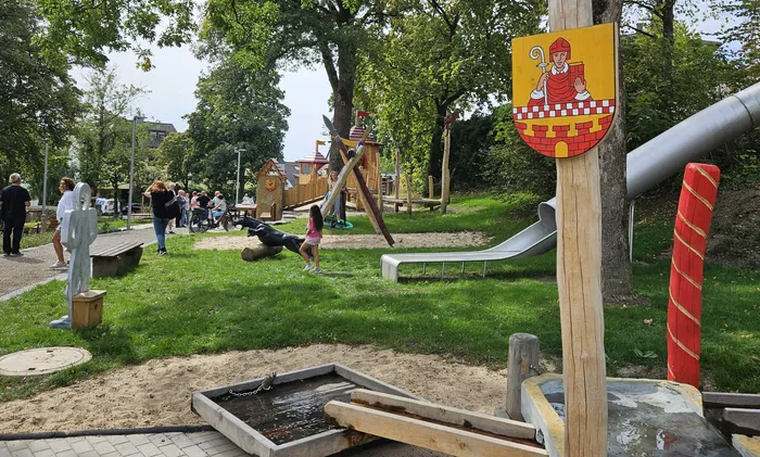 Ein neuer Spielplatz mit Holzspielgeräten, einer Rutsche und einem Sand-Wasser-Spielbereich auf einer Rasenfläche.