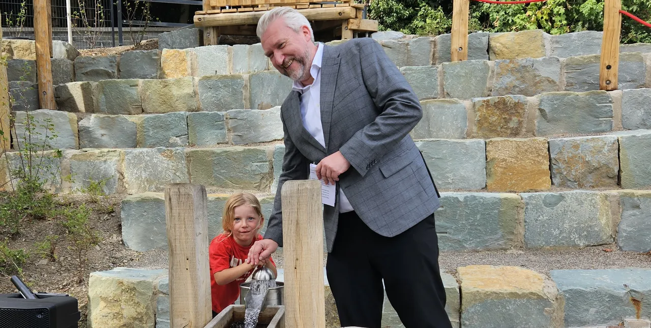 Bürgermeister Sebastian Wagemeyer und ein Kind spielen an einer Wasserinstallation auf dem neu eröffneten Spielplatz.