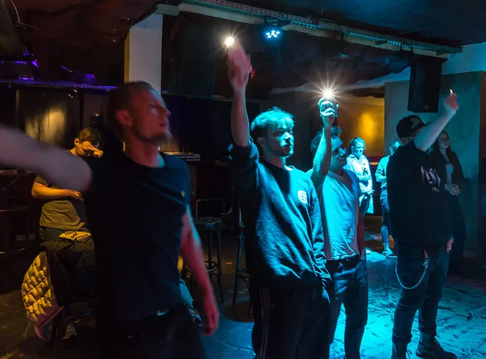 Menschen bei einem Benefizkonzert in einem Club, einige halten ihre Handys mit eingeschaltetem Licht in die Luft.