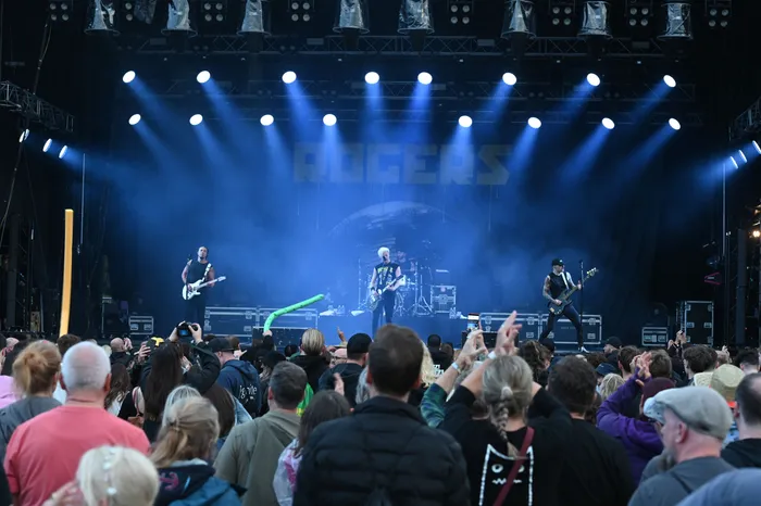 Die Band Rogers spielt auf einer mit blauen Scheinwerfern beleuchteten Bühne vor einem Publikum.