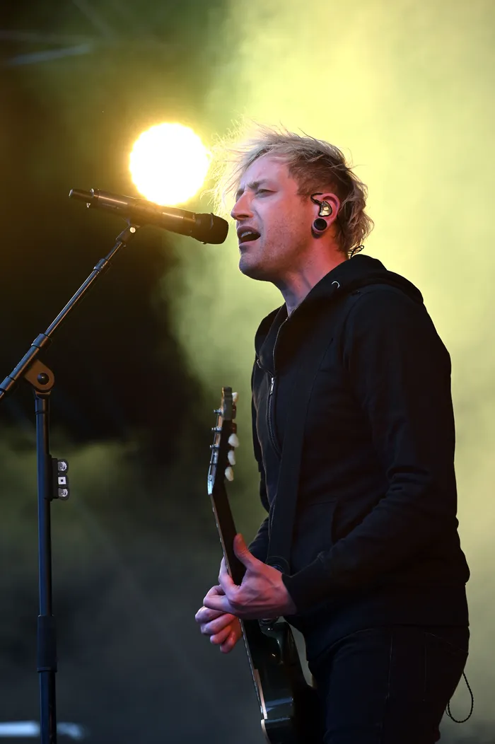 Rogers singt in ein Mikrofon und spielt Gitarre auf einer hell erleuchteten Bühne mit Nebel im Hintergrund.