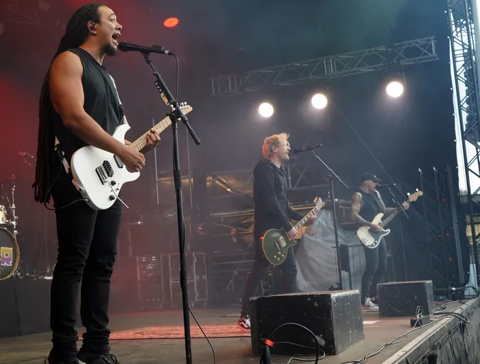 Rogers spielt eine weiße E-Gitarre und singt in ein Mikrofon auf einer beleuchteten Bühne.