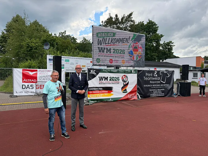 Drei Männer stehen vor einer Werbebande mit dem Aufdruck 