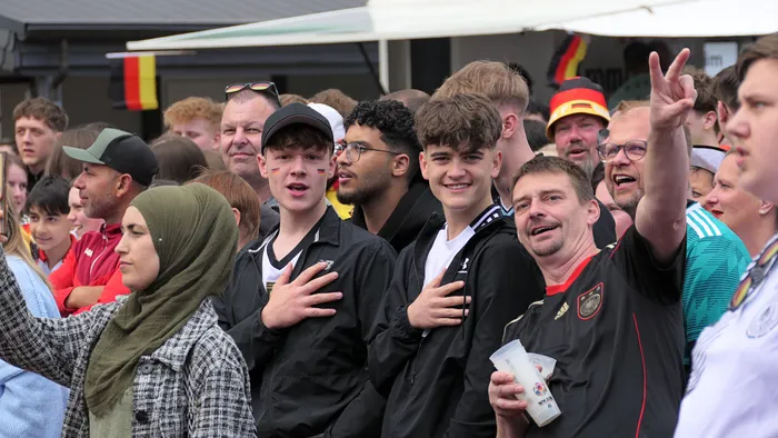 Jubelnde Fans mit Deutschlandfahnen und -trikots feiern den Sieg der deutschen Nationalmannschaft bei der WM-Auftaktpartie gegen Curacao. Im Vordergrund eine Frau mit Kopftuch.