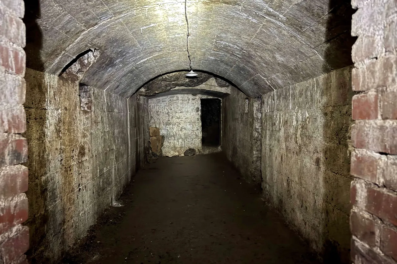 Ein schmaler, gewölbter Gang im Russenbunker der Kluterthöhle, beleuchtet durch eine einzelne hängende Glühbirne.
