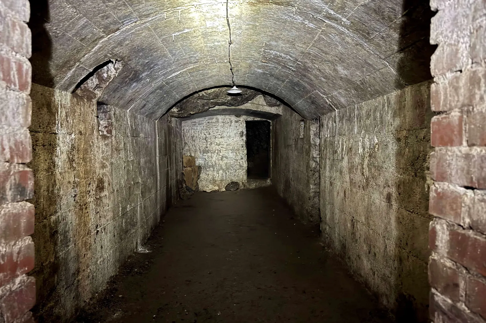 Ein schmaler, gewölbter Gang im Russenbunker der Kluterthöhle, beleuchtet durch eine einzelne hängende Glühbirne.