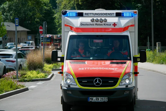 Ein roter Rettungswagen des Deutschen Roten Kreuzes mit Blaulicht fährt auf einer Straße. Im Fahrhaus sitzen zwei Rettungssanitäter.