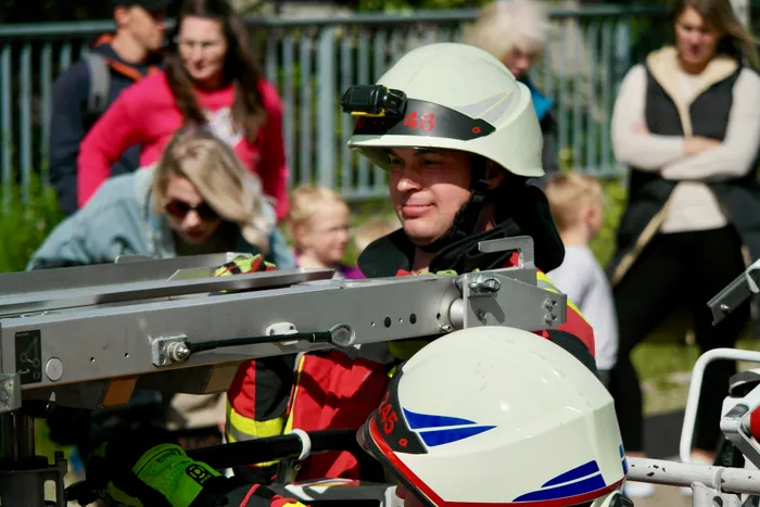Ein Feuerwehrmann in voller Montur mit Helm und Stirnlampe bedient eine hydraulische Rettungsspreizvorrichtung. Im Hintergrund sind verschwommene Zuschauer zu sehen.