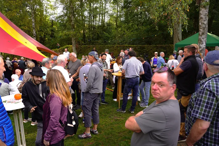 Viele Menschen versammeln sich bei einem Kartoffelfest im Freien auf einer Wiese zwischen Bäumen.
