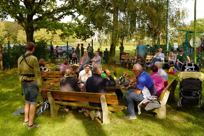 Menschen sitzen an Holztischen im Freien und essen und trinken bei einem Kartoffelfest im Grünen.