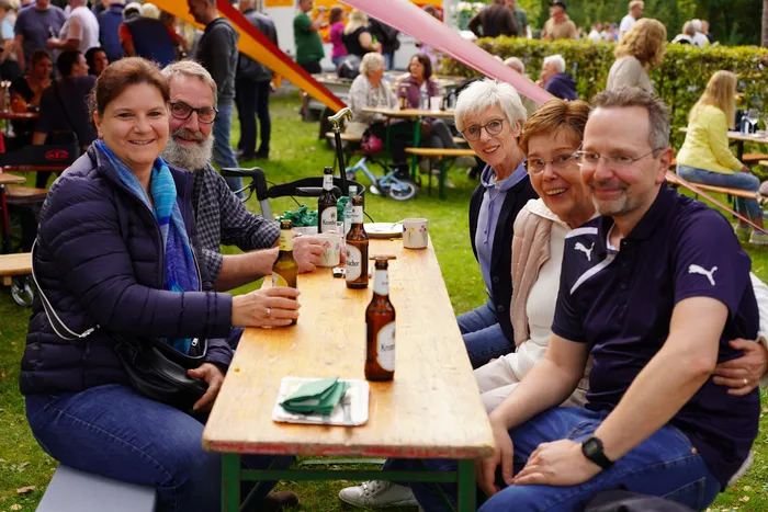 Eine Gruppe von Menschen sitzt an einem langen Holztisch mit Getränken bei einem Kartoffelfest im Freien.