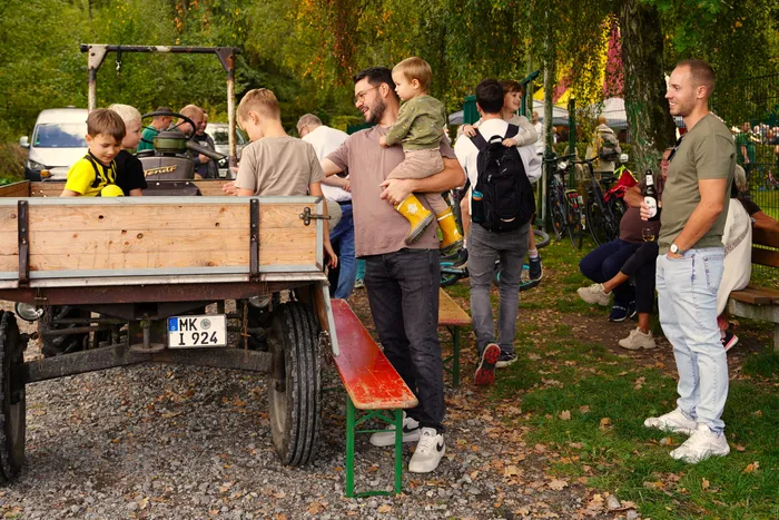 Ein Mann hält ein Kleinkind auf dem Arm, im Vordergrund steht ein hölzerner Anhänger bei einem Kartoffelfest.
