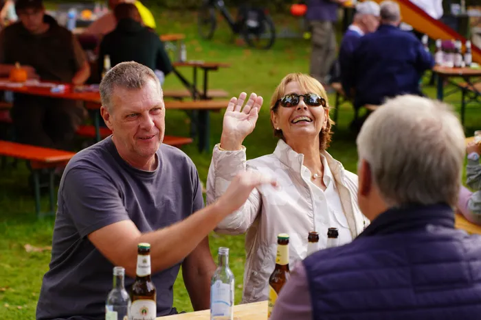 Ein Mann und eine lachende Frau mit Sonnenbrille sitzen an einem Tisch bei einem Kartoffelfest im Freien.