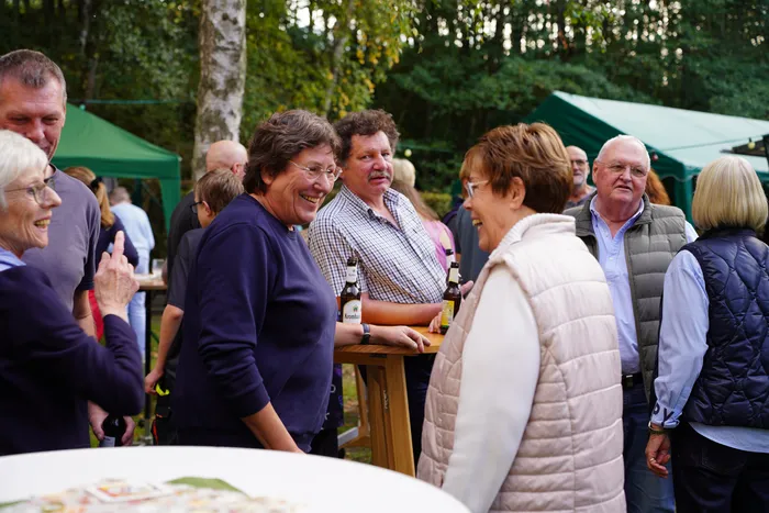 Besucher unterhalten sich bei einem Kartoffelfest im Freien an Stehtischen vor einem grünen Zelt.