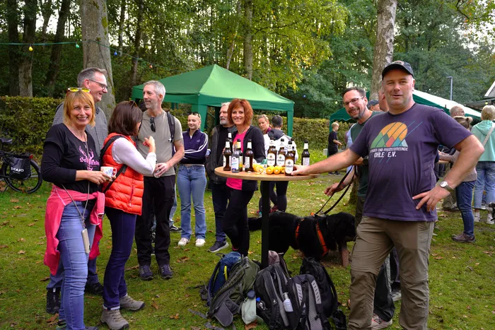 Eine Gruppe von Menschen steht bei einem Kartoffelfest im Freien vor einem grünen Zelt an einem Tisch mit Getränken.