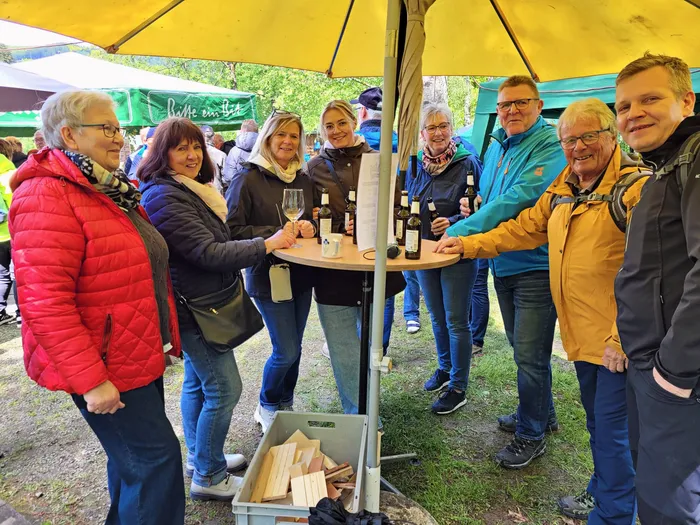 Eine Gruppe von Menschen steht um einen Tisch mit Weinflaschen unter einem gelben Zelt. Sie probieren Wein und unterhalten sich bei einer Veranstaltung des SGV Elsetal.