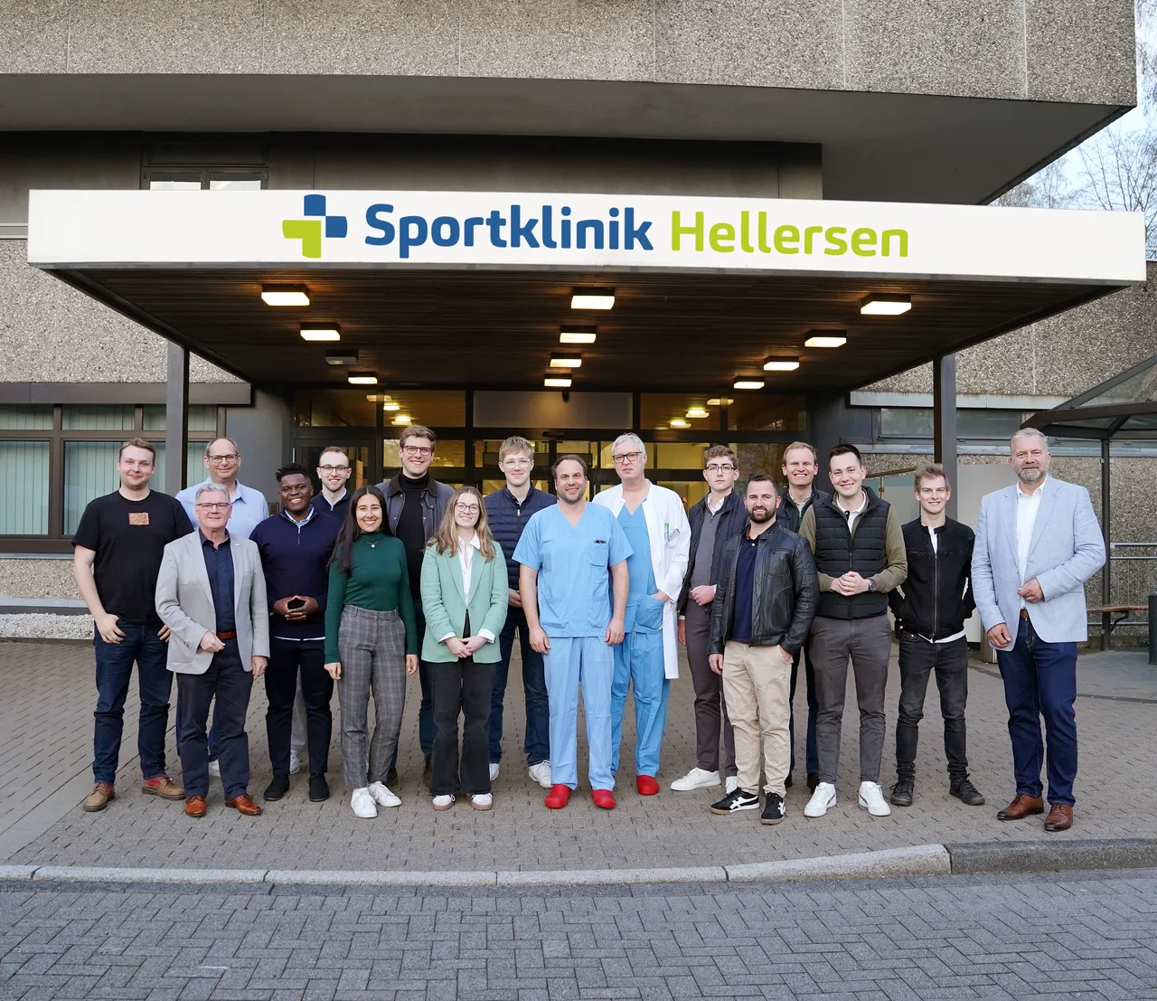 Gruppe von etwa zwanzig Personen vor dem Eingang der Sportklinik Hellersen, darunter ein Mann in OP-Kleidung. Im Hintergrund ein Schild mit dem Kliniknamen.