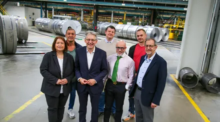 Gruppe von sieben Personen posiert vor großen Metallrollen in einer Fabrikhalle. Von links: Bettina Lugk, Manuel Jimenez, Achim Post, Fabian Ferber, Jörg Lohölter, Tanju Yoldasoglu und Michael Scheffler.