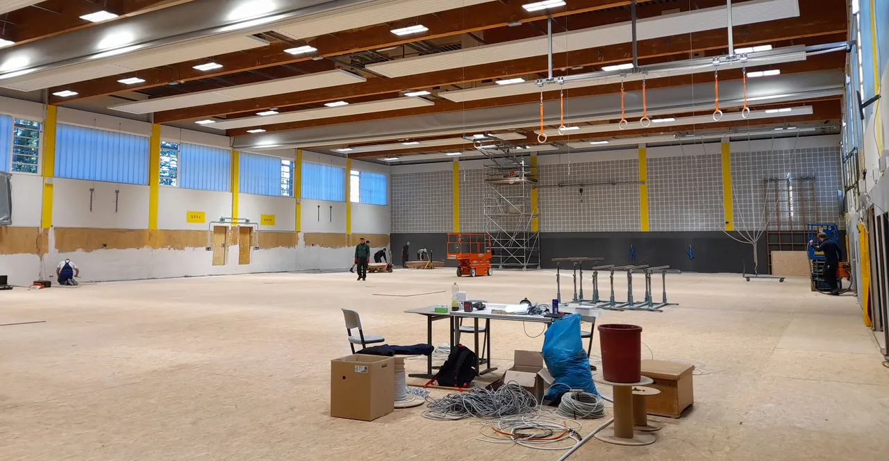 Innenansicht der Sporthalle des Zeppelin-Gymnasiums während der Sanierungsarbeiten mit Baumaterialien, Gerüsten und Arbeitern.