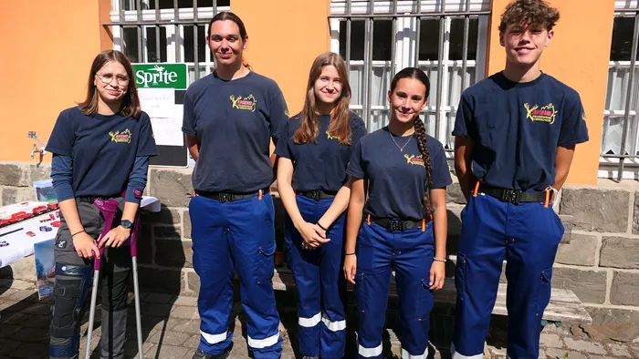 Fünf junge Menschen in der Uniform der Feuerwehr Hüinghausen stehen nebeneinander vor einem Gebäude, eine Person nutzt Krücken.