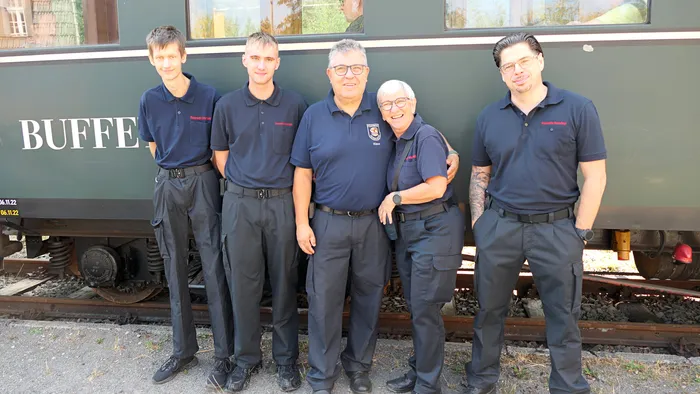 Fünf Männer in dunkelblauen Uniformen stehen lächelnd vor einem dunkelgrünen Waggon mit der Aufschrift „BUFFET“.