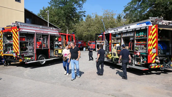 Zwei Feuerwehrfahrzeuge mit geöffneten Seitenfächern, die verschiedene Ausrüstungsgegenstände zeigen, umgeben von Besuchern.