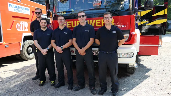 Fünf Männer in dunkelblauen Poloshirts der Feuerwehr Plattberg stehen vor einem roten Feuerwehrfahrzeug.