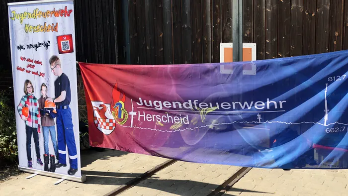 Banner der Jugendfeuerwehr Herscheid, bestehend aus einem vertikalen Roll-up mit Fotos von Jugendlichen und einem großen horizontalen Banner mit Logo.