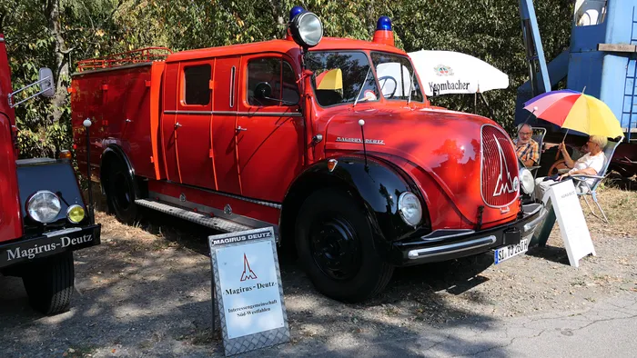 Ein rotes historisches Magirus-Deutz Löschfahrzeug steht auf einem Schotterplatz.