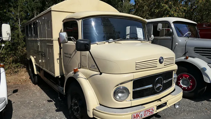 Ein cremefarbenes, historisches Mercedes-Benz Löschfahrzeug steht neben einem grauen Oldtimer-LKW.