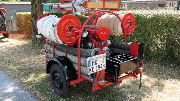 Roter historischer Feuerwehr-Anhänger mit aufgerollten weißen Schläuchen, einem Motor und dem Kennzeichen MK KO 1948.
