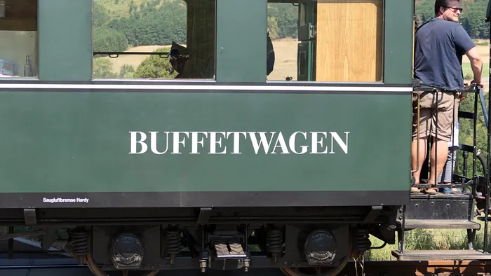 Grüner Buffetwagen einer Museumseisenbahn mit der weißen Aufschrift „BUFFETWAGEN“. Ein Mann steht auf der Plattform am rechten Bildrand.