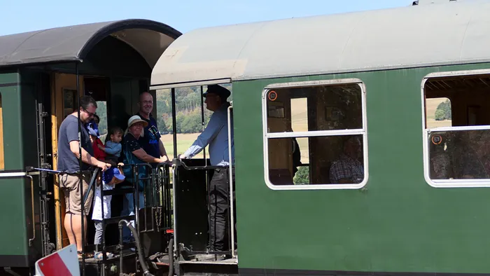 Besucher und ein Bahnmitarbeiter stehen auf der Plattform eines grünen historischen Eisenbahnwagens.