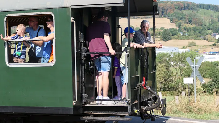 Besucher blicken aus den Fenstern und von der offenen Plattform eines grünen historischen Eisenbahnwagens.