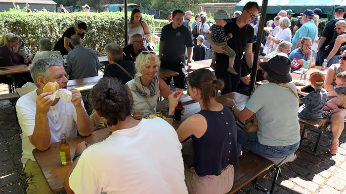 Besucher sitzen an Holztischen im Freien und essen und trinken beim Blaulichttag in Hüinghausen.