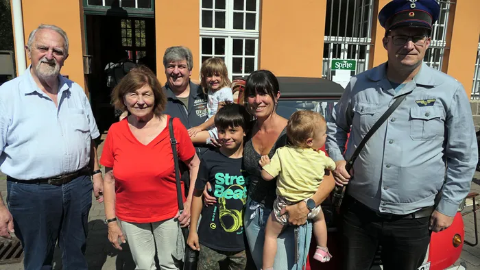 Eine Gruppe von Menschen unterschiedlichen Alters posiert vor einem Gebäude und einem Fahrzeug beim Blaulichttag.