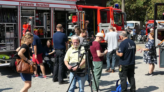Besucher und ein Kameramann stehen vor einem roten Feuerwehrfahrzeug der Feuerwehr Herscheid beim Blaulichttag in Hüinghausen.