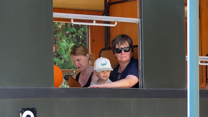 Eine Frau, ein kleiner Junge mit weißer Kappe und eine Frau mit Sonnenbrille sitzen in einem Waggon der Museumseisenbahn.