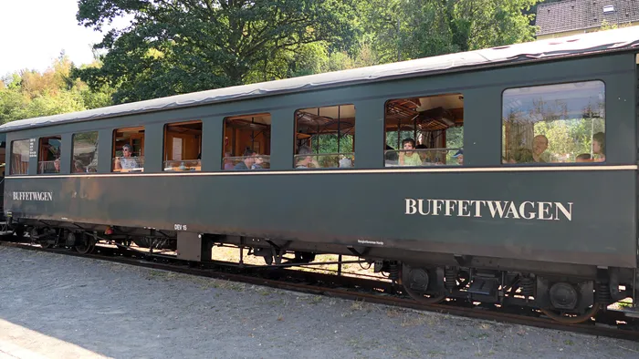 Ein dunkelgrüner Buffetwagen einer Museumseisenbahn mit Passagieren in den Fenstern.