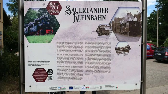Eine historische Dampflokomotive fährt auf einer Schmalspurstrecke durch eine ländliche Landschaft, umgeben von Zuschauern.