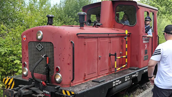 Rote Lokomotive der Sauerländer Kleinbahn steht auf Gleisen, ein Mann in Uniform steht daneben.