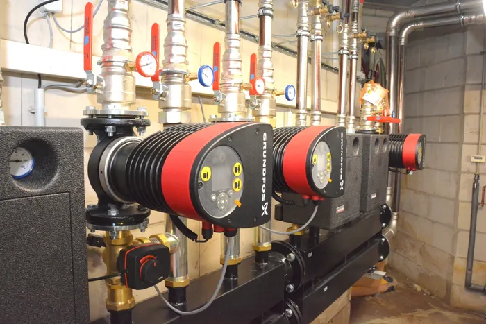 Mehrere Grundfos-Umwälzpumpen an einem System aus silbernen Rohren, roten Ventilen und Manometern.