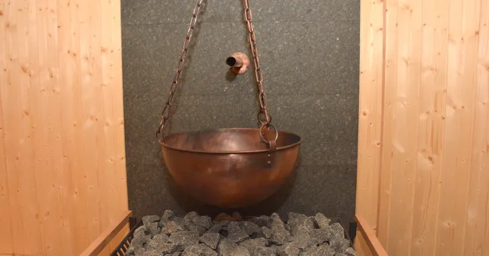 Ein Kupferkessel hängt an Ketten über Saunasteinen in einer Bio-Sauna.