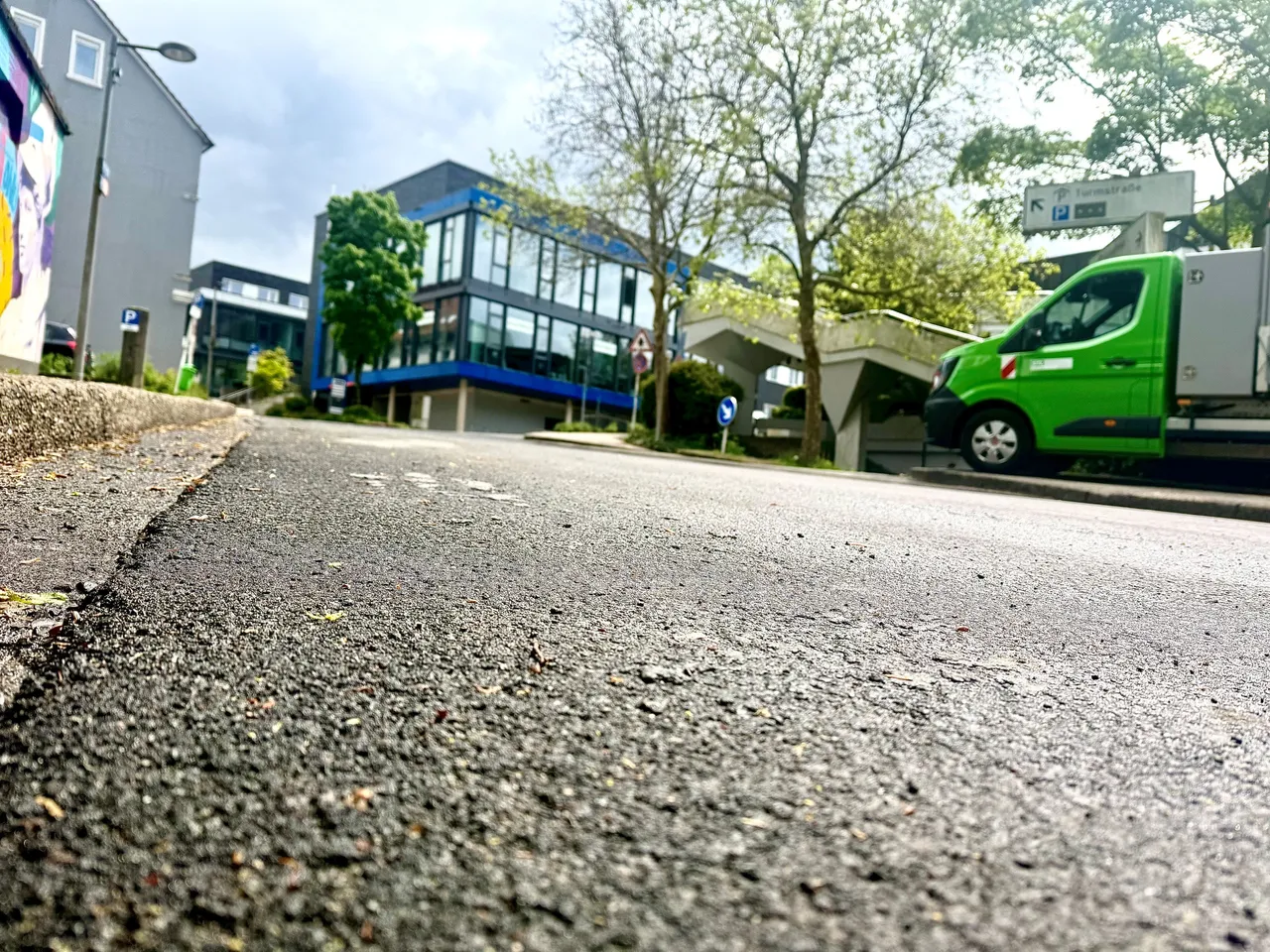 Blick auf die Schillerstraße mit einem grünen Lieferwagen am Straßenrand und modernen Bürogebäuden im Hintergrund. Ein Tempolimit-Schild weist auf eine verkehrsberuhigte Zone hin.