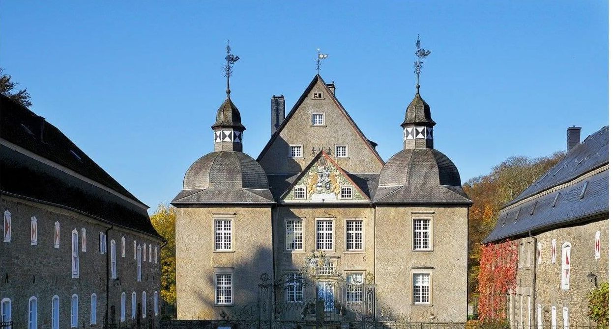 Das barocke Wasserschloss Neuenhof mit zwei markanten Türmen und einem zentralen Giebel unter blauem Himmel.